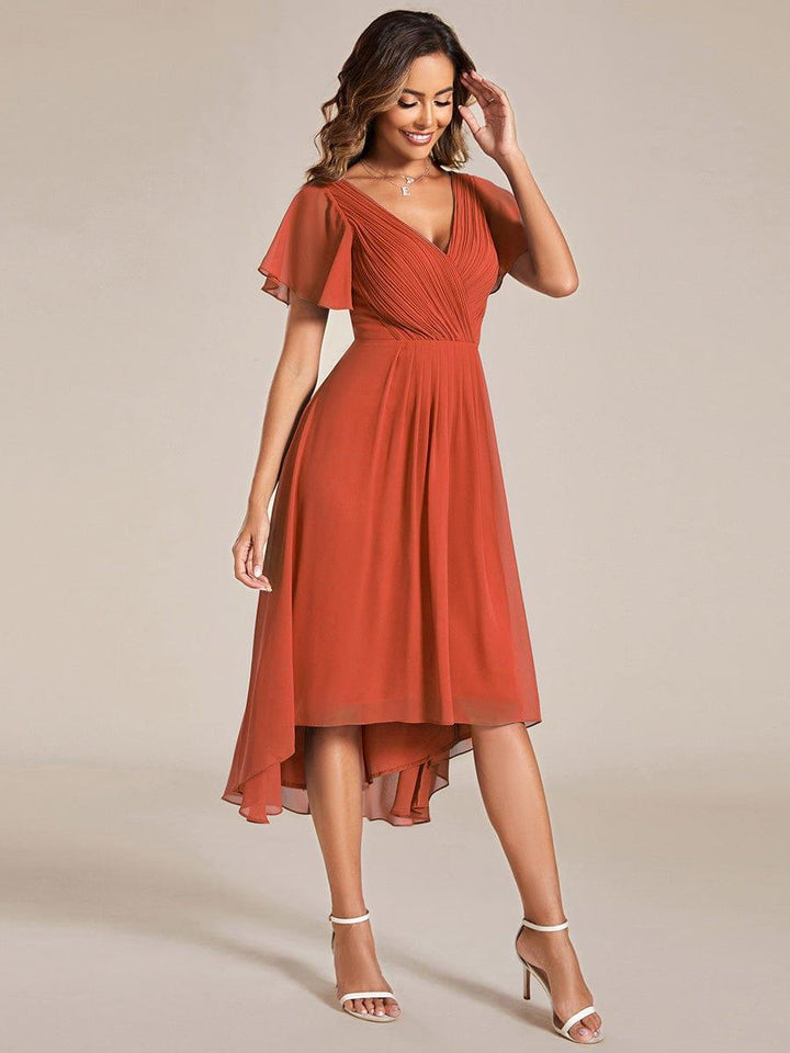 Lachend model in terracottakleurige jurk, driekwartsaanzicht, met één hand bij het haar en wijd uitlopende chiffon rok. 96