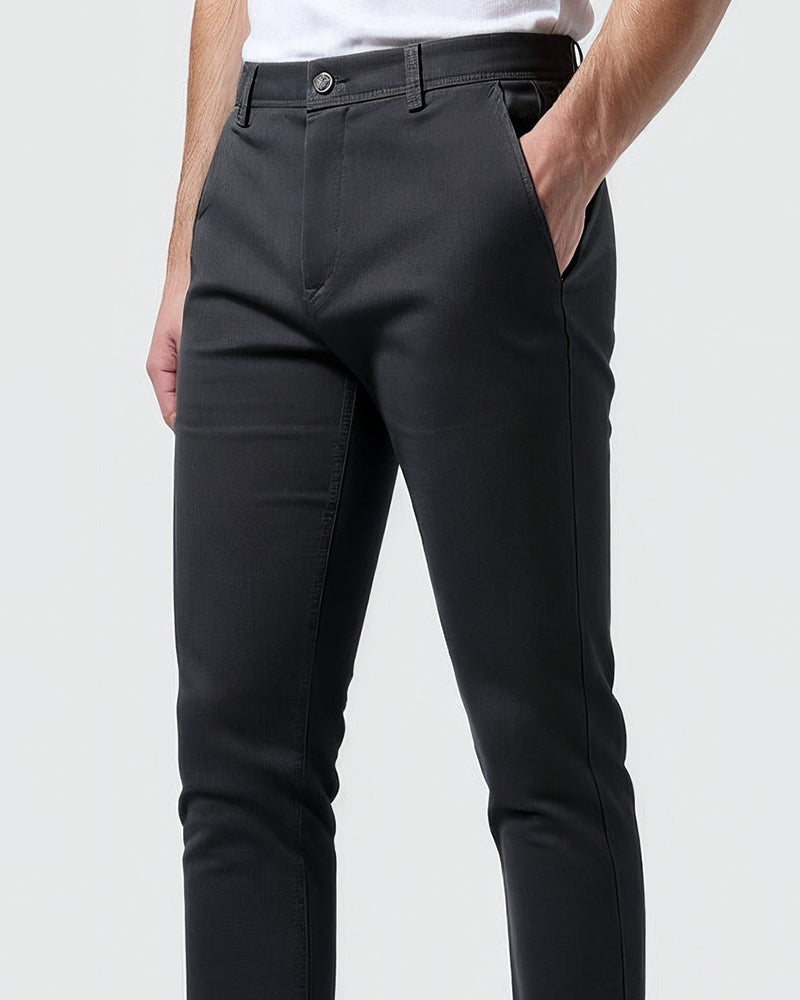 Close-up van het middenstuk van de donkergrijze chino met knoop, riemlussen en een hand in de zak. 10