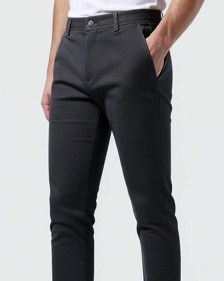 Close-up van het middenstuk van de donkergrijze chino met knoop, riemlussen en een hand in de zak. 10