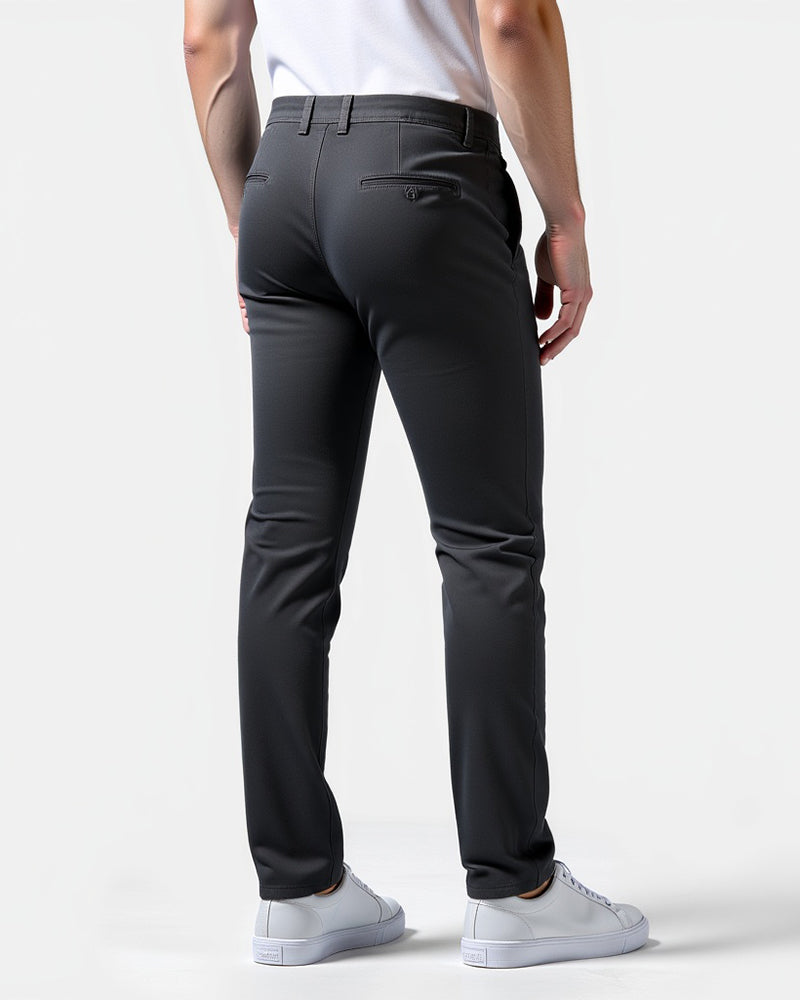 Achterkant van de donkergrijze chino met paspelzak met knoopje, gedragen door een model in witte sneakers. 8