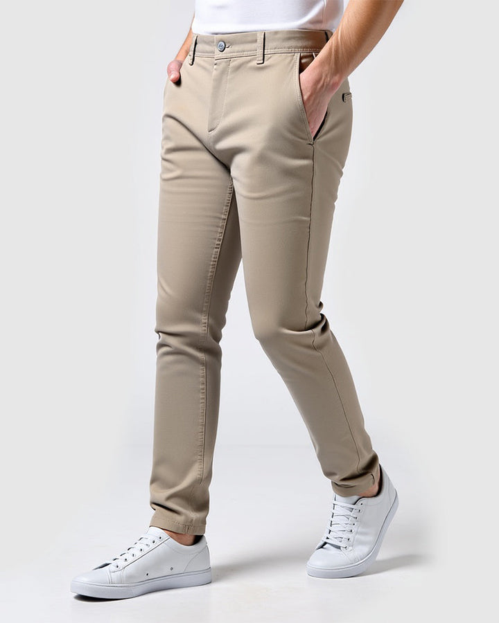 Beige chino schuin van voren gedragen door een model met witte sneakers en handen in de zakken. 14