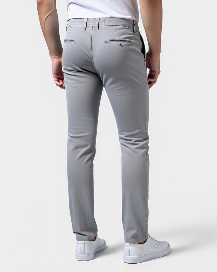 Achterkant van de lichtgrijze chino met twee paspelzakken, gedragen door een model in witte sneakers. 3