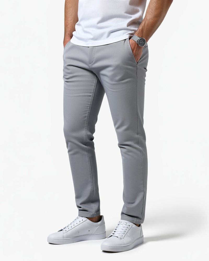 Lichtgrijze slim fit chino, schuin van voren gedragen door een model met witte sneakers en een hand in de zak. 1