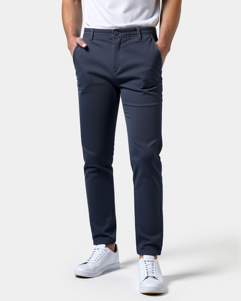 Donkerblauwe chino van voren gedragen met wit shirt en witte sneakers, beide handen in de zakken. 15
