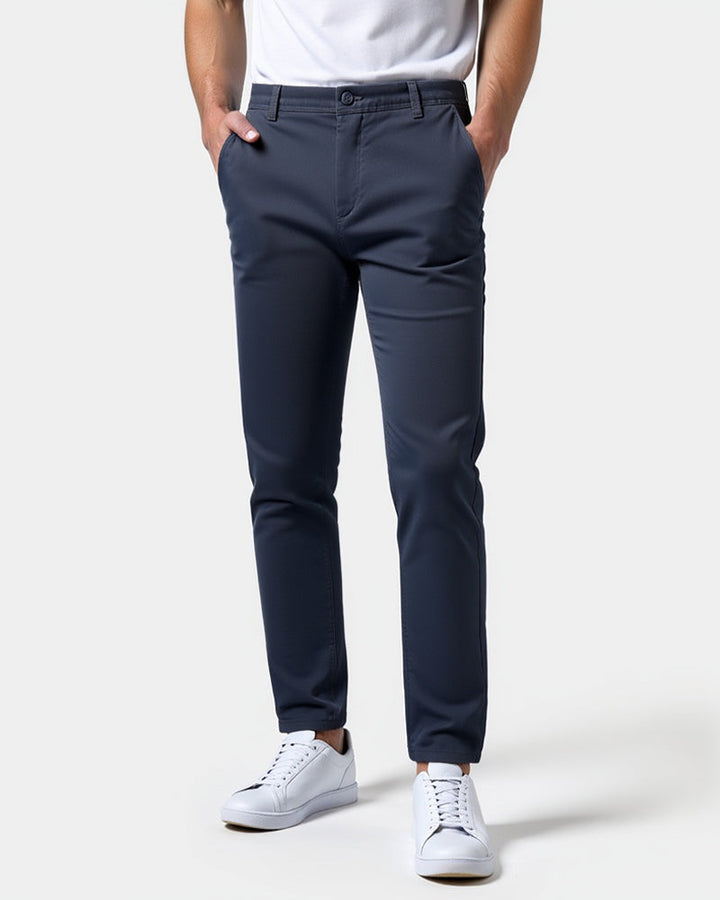 Donkerblauwe chino van voren gedragen met wit shirt en witte sneakers, beide handen in de zakken. 15