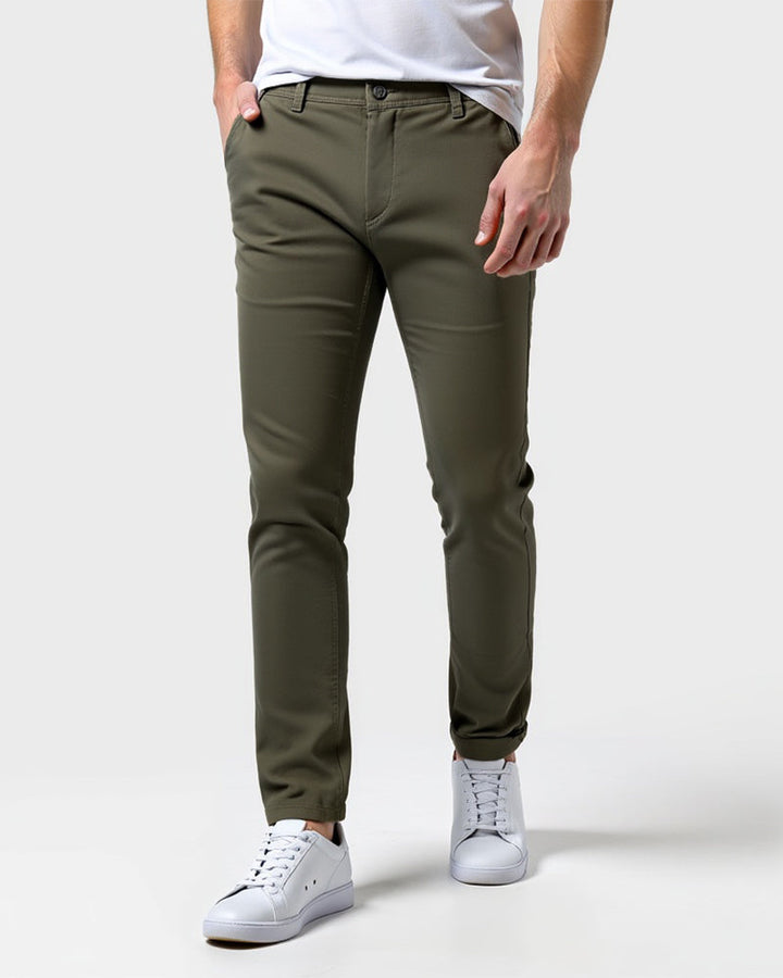 Olijfgroene chino van voren gedragen met wit shirt en witte sneakers, één hand in de zak. 13