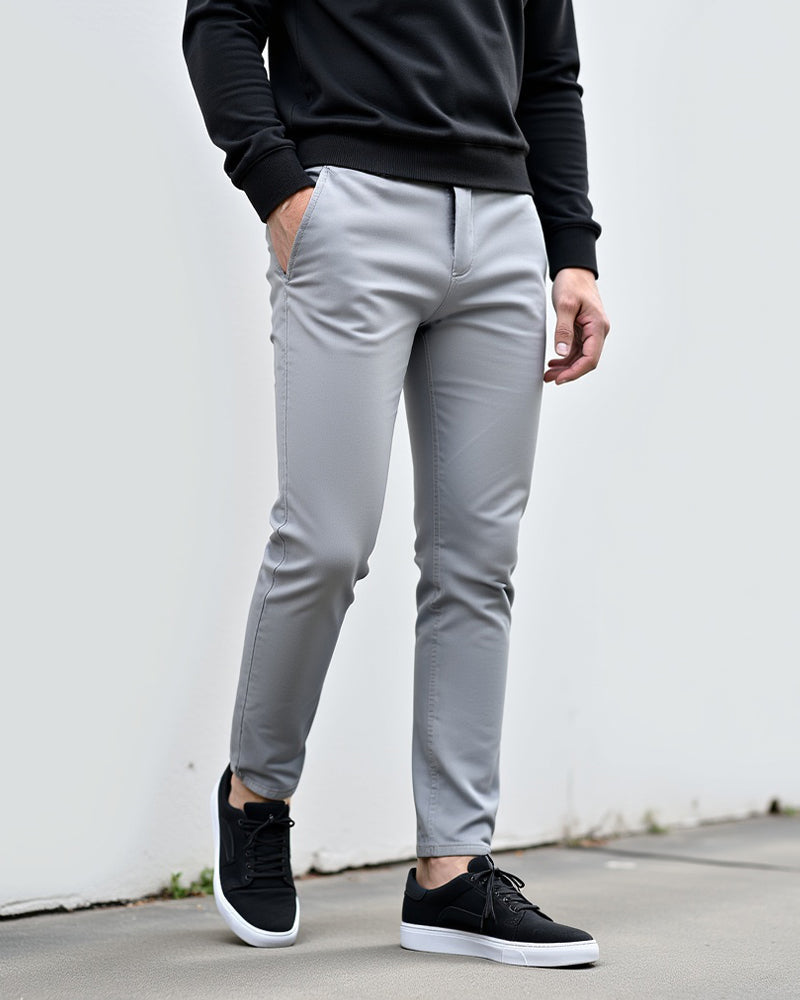 Lichtgrijze chino buiten gedragen voor een witte muur, gecombineerd met een zwarte trui en zwarte sneakers. 2