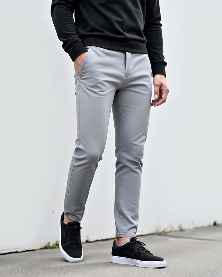 Lichtgrijze chino buiten gedragen voor een witte muur, gecombineerd met een zwarte trui en zwarte sneakers. 2