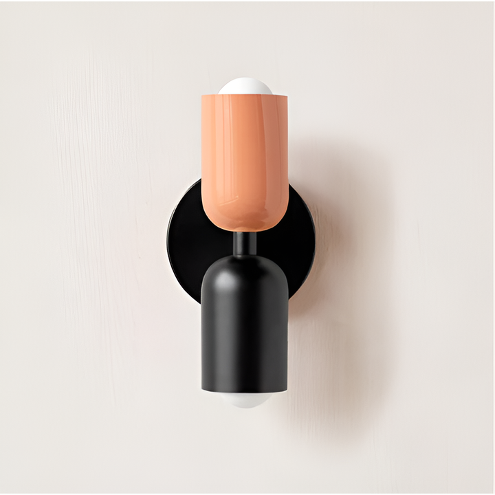 Wandlamp met perzik-oranje bovenkap en zwarte onderkap op een zwarte ronde plaat, tegen een lichte muur. 23