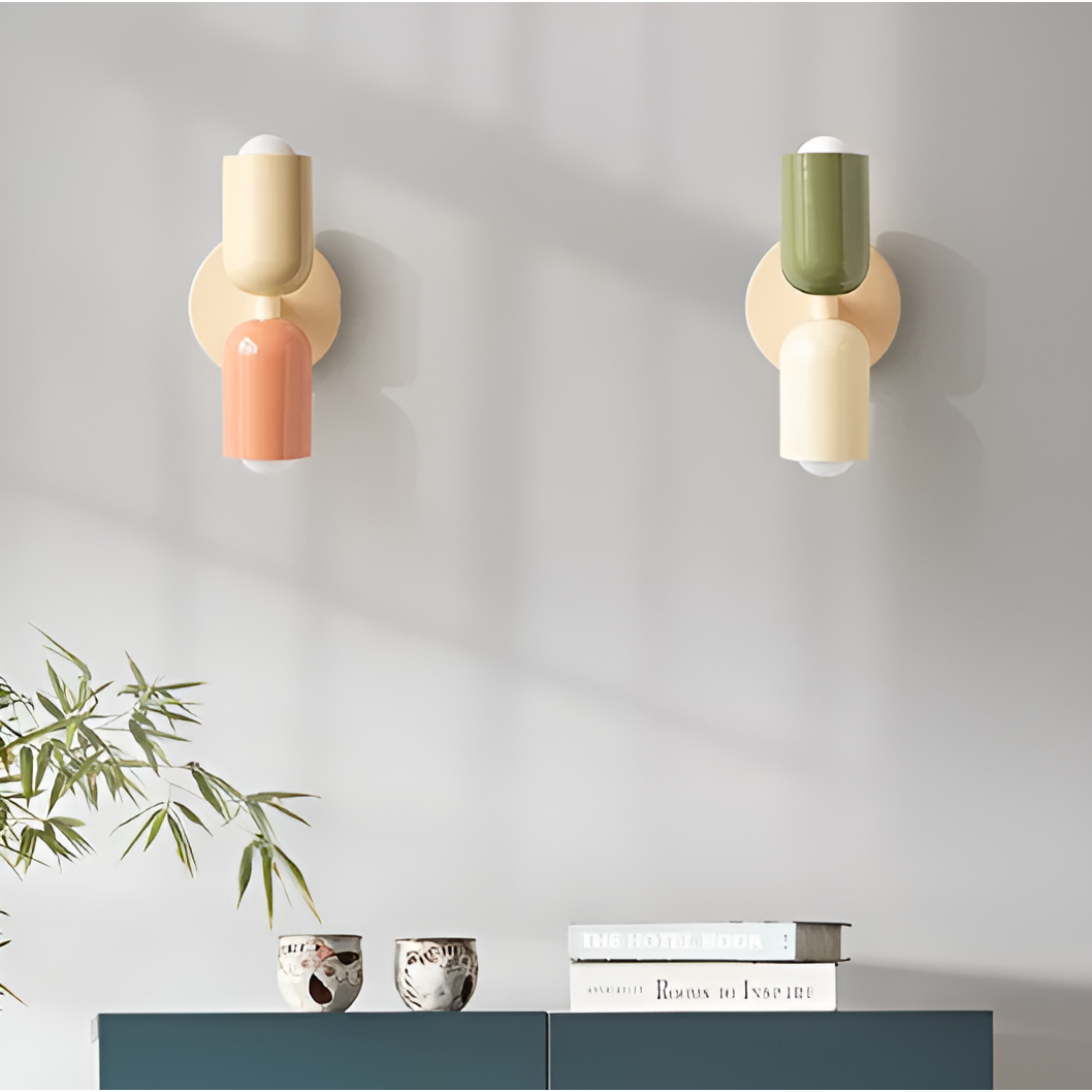 Twee wandlampen met crème wandplaat aan een grijze muur boven een kastje, links perzik met crème, rechts groen met crème. 2