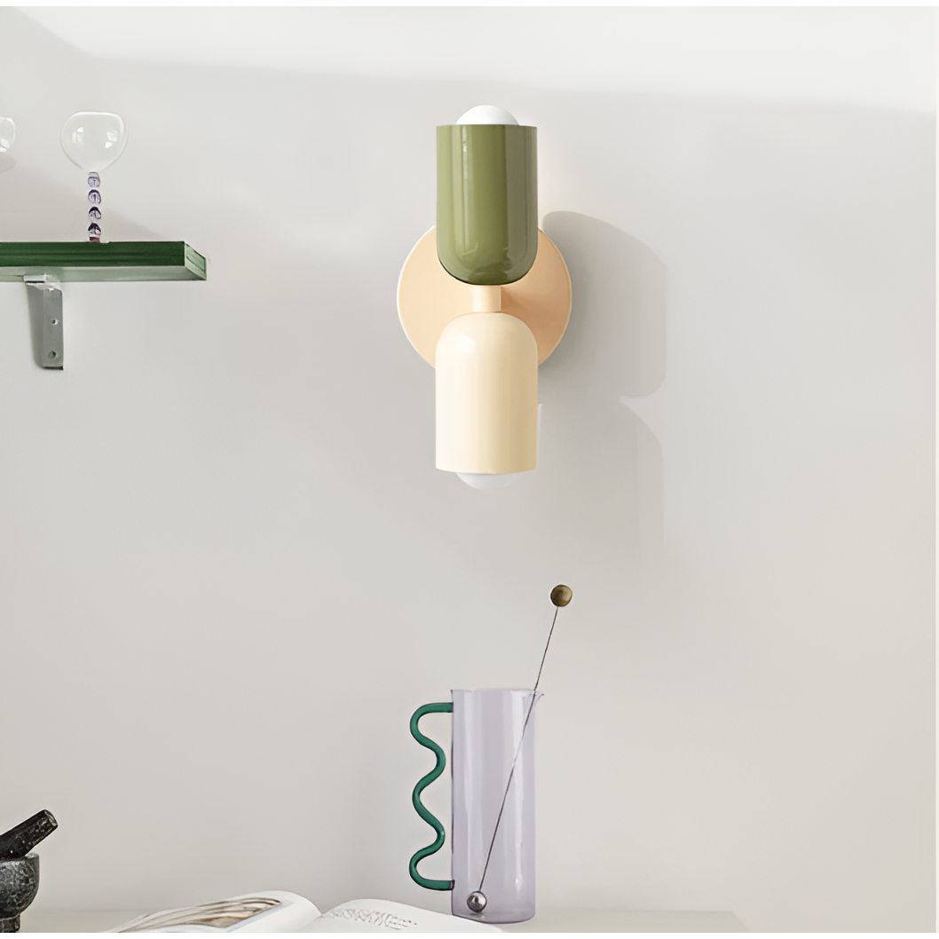 Groen-crème wandlamp opgehangen in een interieur met plank, glazen karaf met golvend handvat en opengeslagen boek. 35