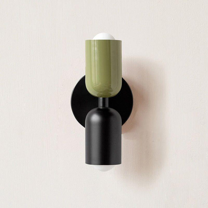 Wandlamp met groene bovenste lichtkop en mat zwarte onderste lichtkop op een zwarte wandplaat. 12
