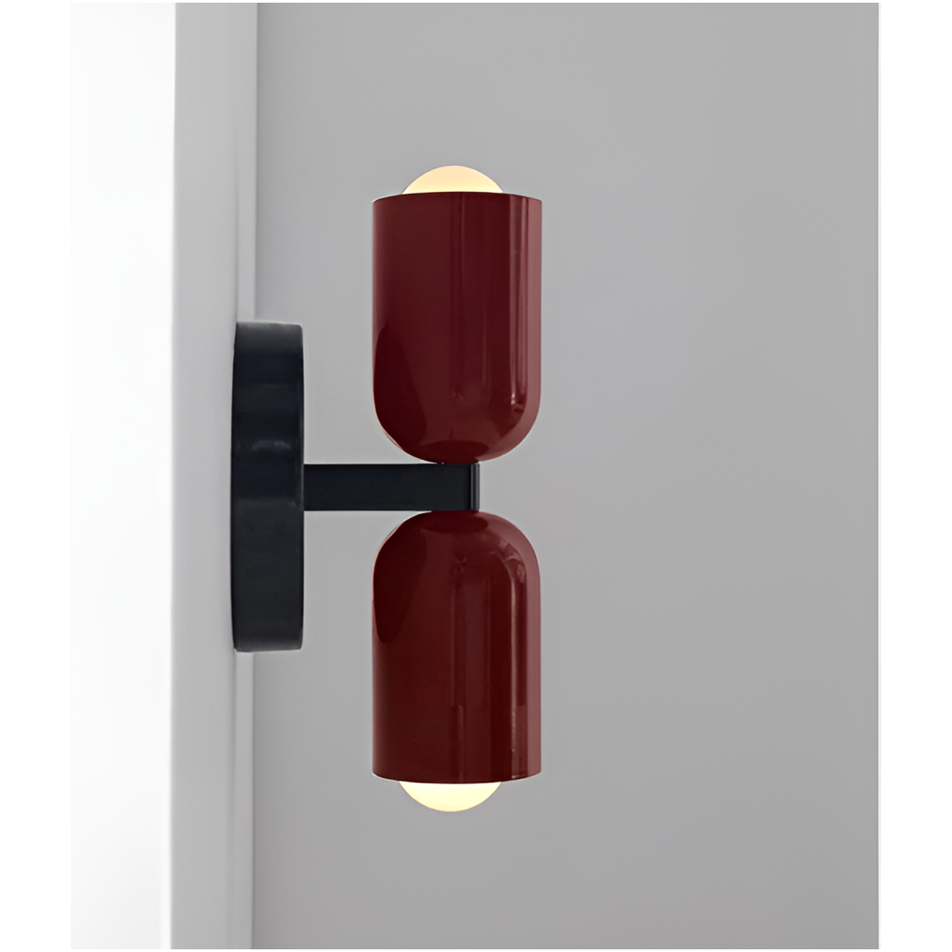 Zijaanzicht van een wandlamp met twee donkerrode lichtkoppen en zwarte arm, die de afstand tot de muur toont; de lampen branden. 17