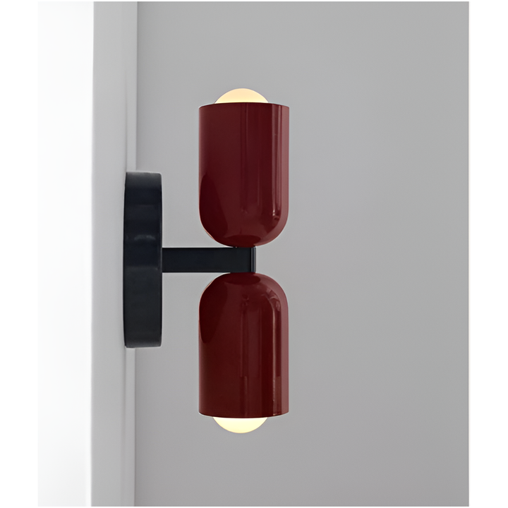 Zijaanzicht van een wandlamp met twee donkerrode lichtkoppen en zwarte arm, die de afstand tot de muur toont; de lampen branden. 17
