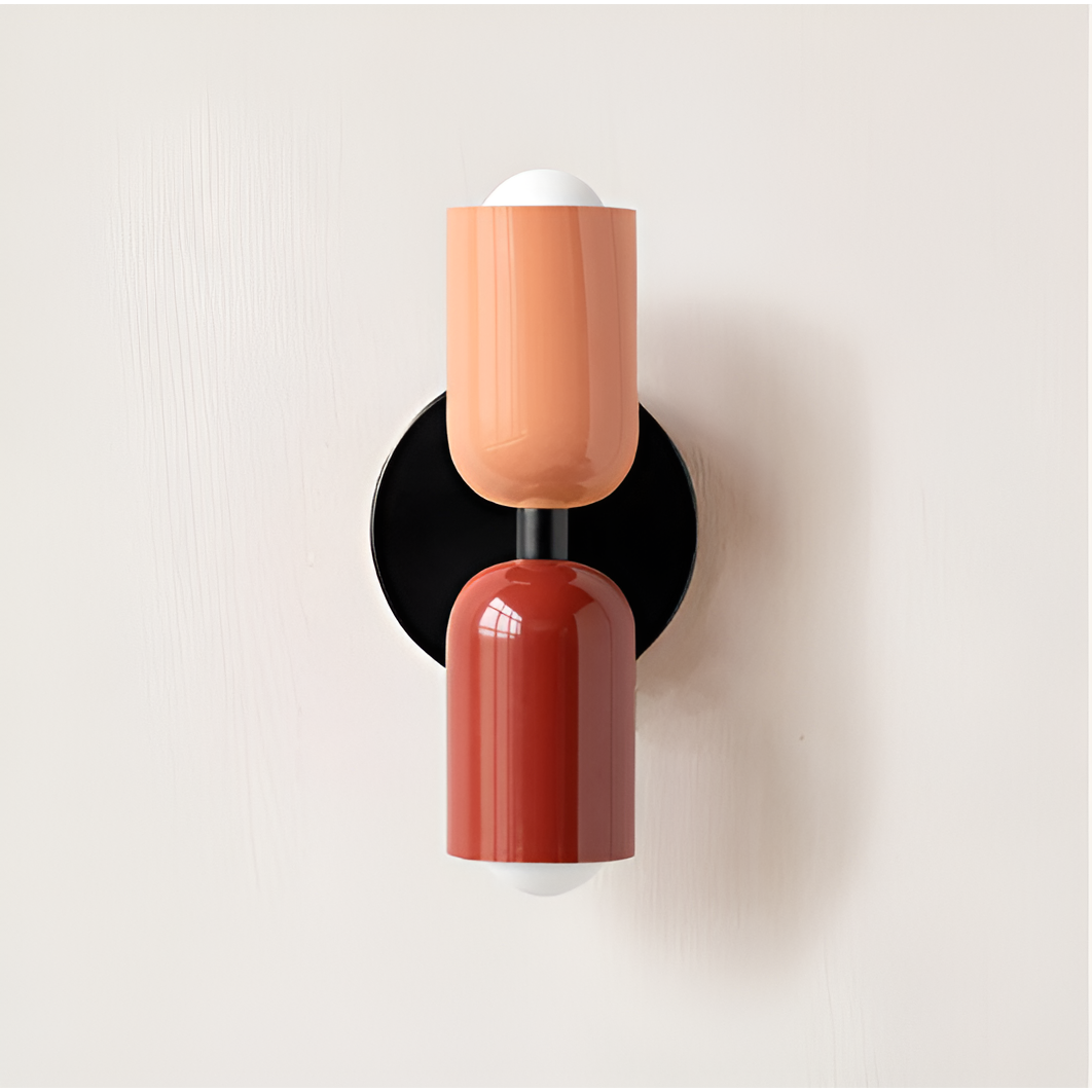 Wandlamp met perzikkleurige bovenste lichtkop en rode onderste lichtkop op een ronde zwarte wandplaat. 18