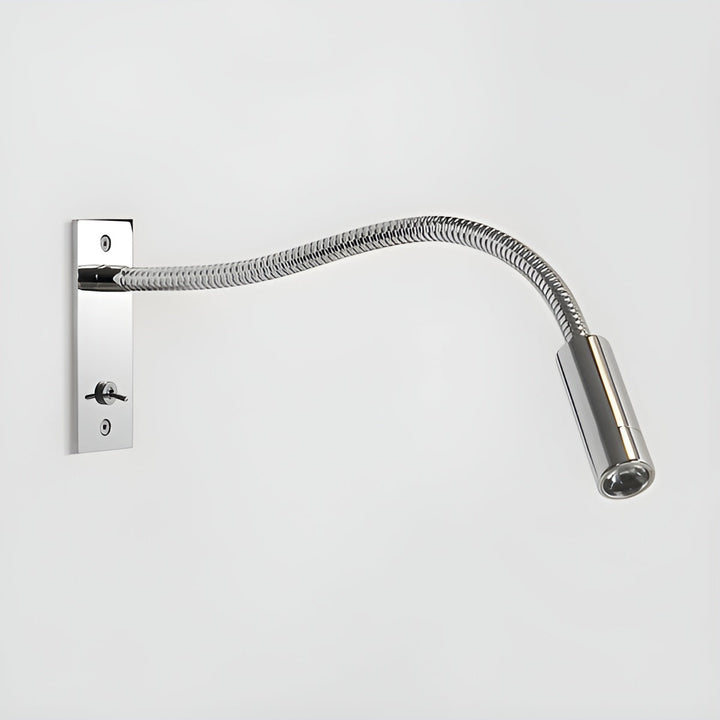 Wandlamp in glanzend gepolijst chroom met gegolfde flexibele arm, tuimelschakelaar en cilindrische lampkop tegen een lichte muur. 12