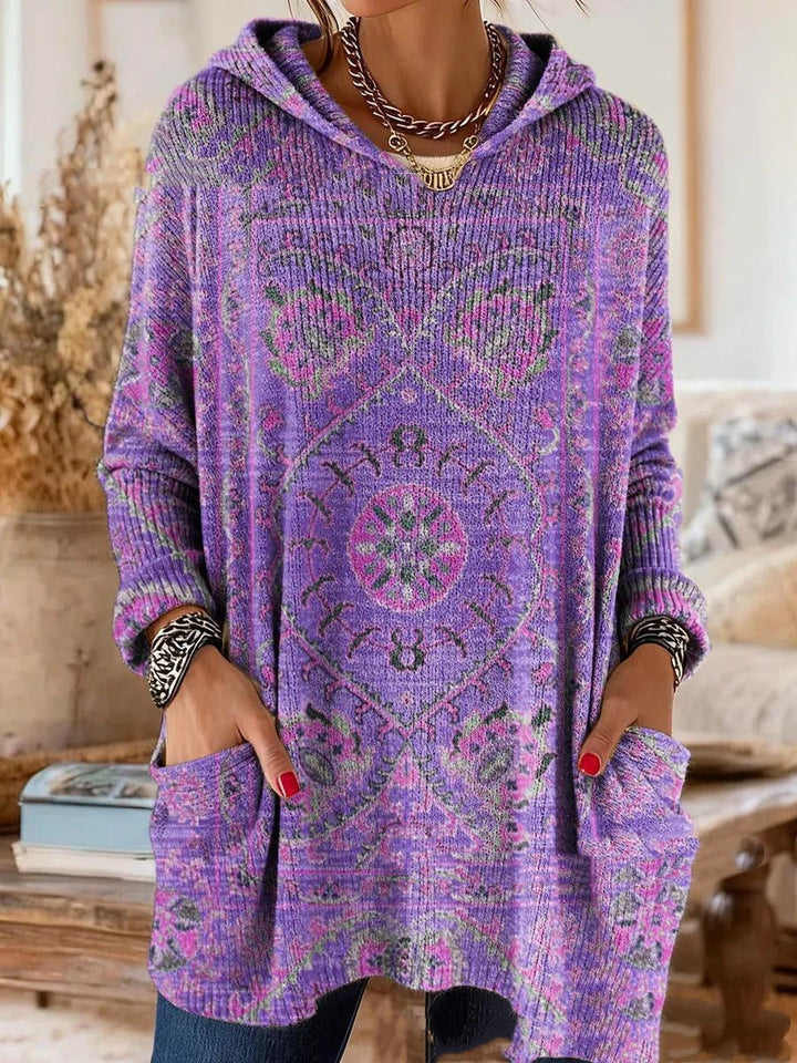 Dezelfde tuniek in paars met roze en groen medaillonmotief, gedragen door een model met de handen in de zakken. 2