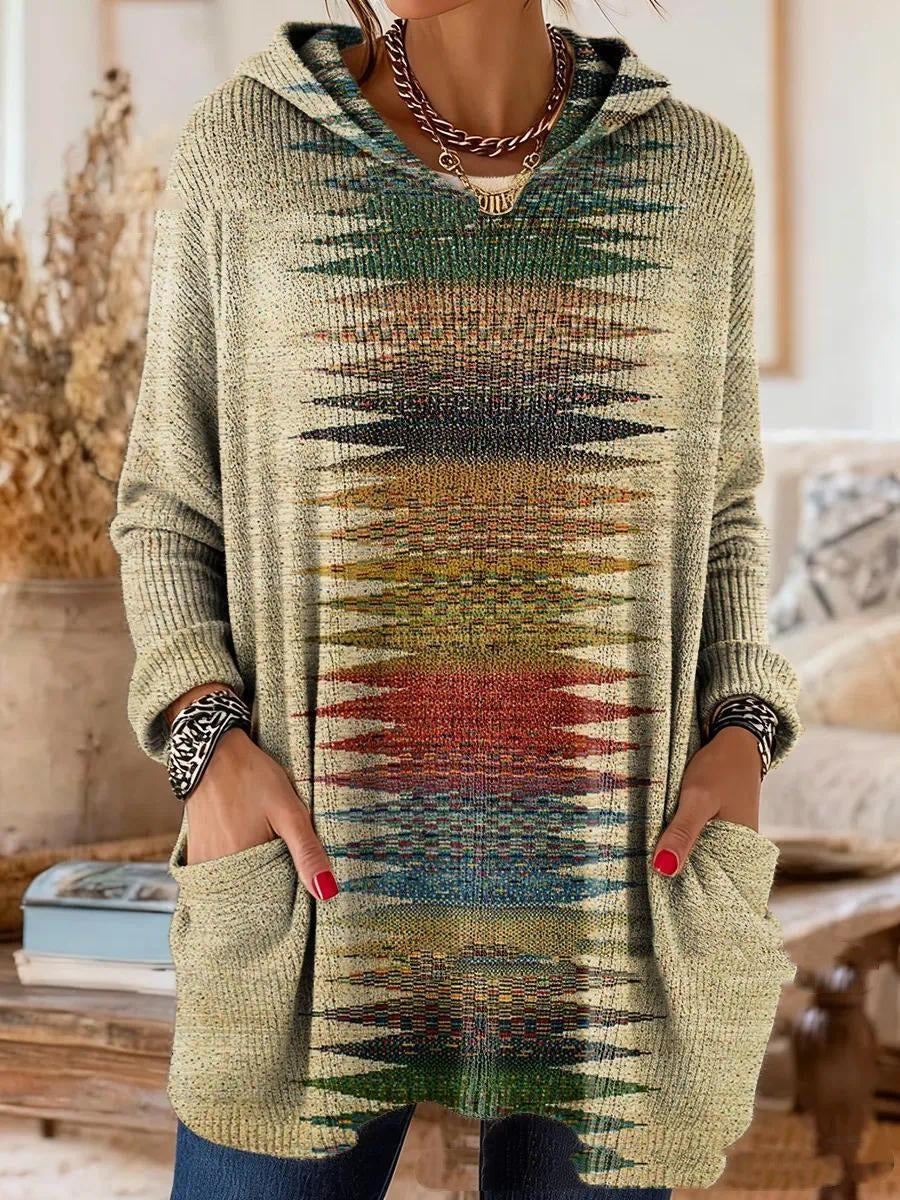 Beige gebreide tuniek met een verticale band van kleurrijke puntige vormen, gedragen door een model met handen in de zakken. 5