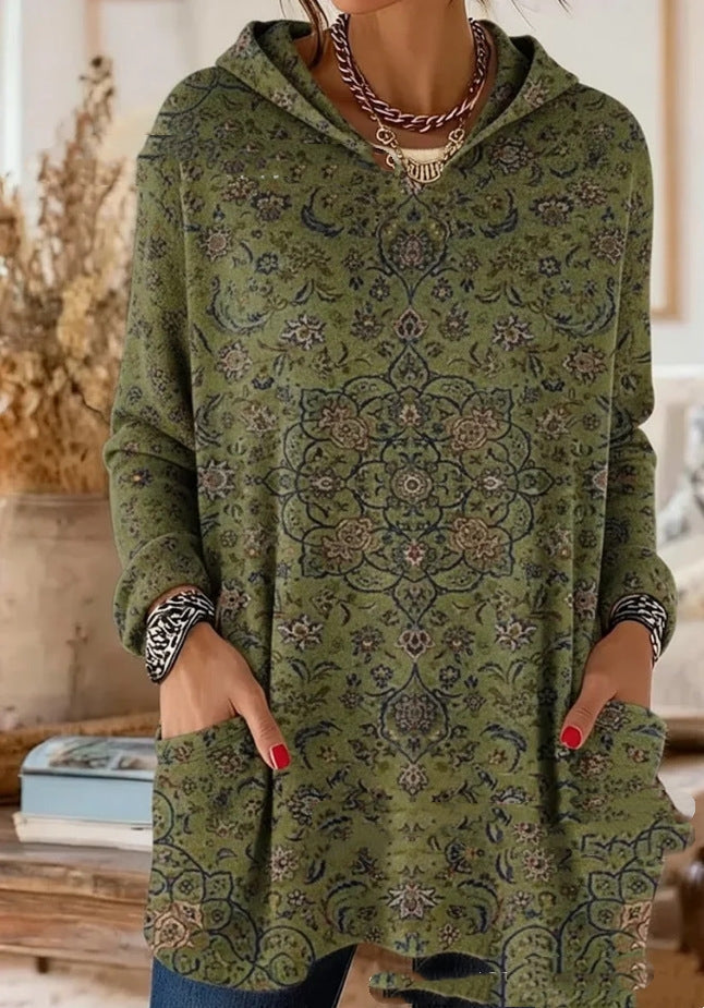 Groene tuniek met fijn donker bloemenmotief, gedragen door een model met de handen in de opgestikte zakken. 7