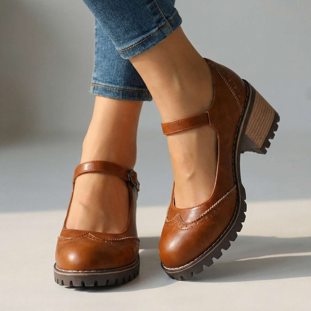 Cognacbruine Mary Jane-schoenen met brogue-details en enkelbandje, gedragen met een spijkerbroek op een lichte vloer 2