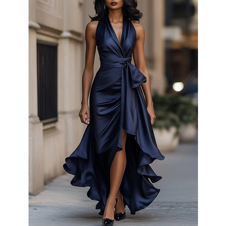 Voorkant van de marineblauwe satijnachtige maxi-jurk met halternek en strik in de taille, gedragen door een model op straat. 1