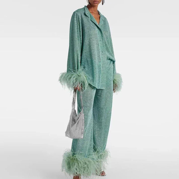 Model draagt de set in mintgroen glitter met reverskraag, veren aan manchetten en broekspijpen en een zilveren tas in de hand. 2