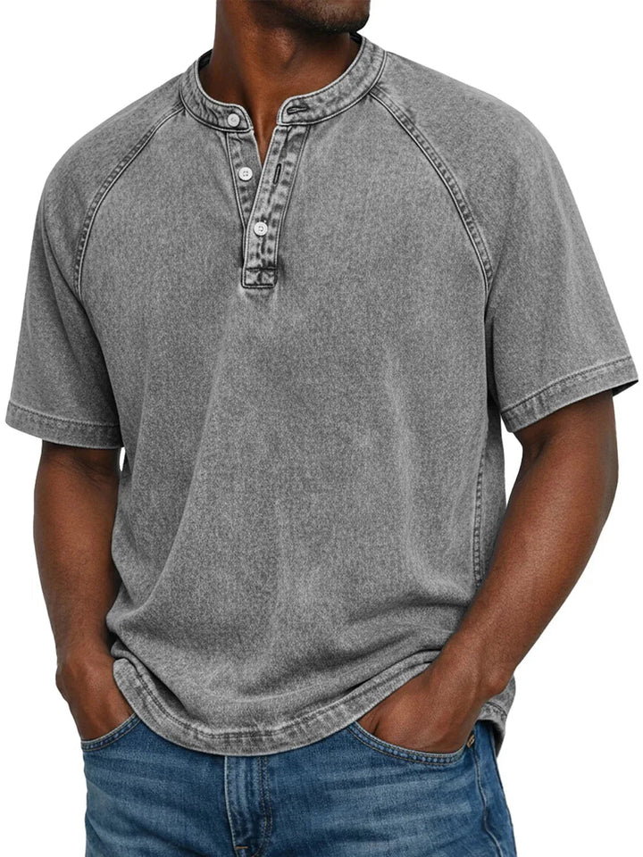 Man draagt het gewassen Henley-shirt met korte raglanmouwen in grijs, met handen in de broekzakken. 4
