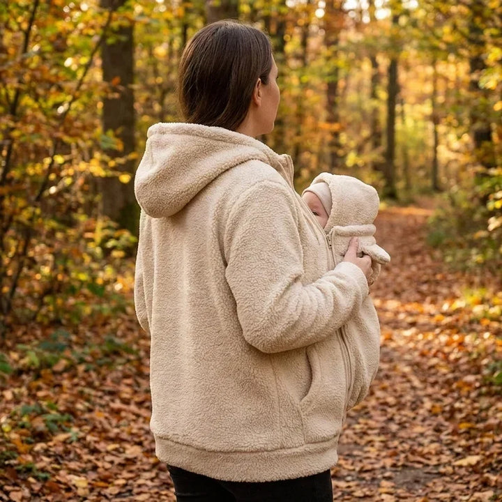 Moeder in beige sherpa hoodie gezien van opzij tijdens een herfstwandeling, met haar baby in het voorpaneel met capuchon. 6