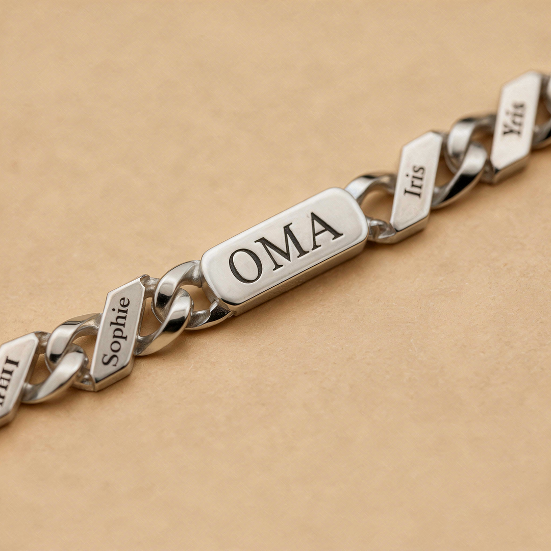 Close-up van het gegraveerde middenplaatje en omliggende naamschakels van de zilverkleurige armband op een beige ondergrond. 8