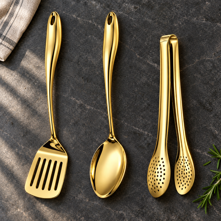 Gouden spatel met gleuven, lepel en tang met gaatjes op een donkere steenplaat met linnen doek en rozemarijn. 23