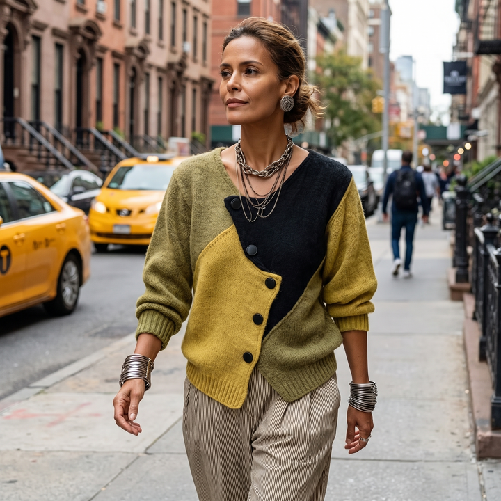 Model loopt buiten op straat in de trui met gestreepte pantalon, met schuine knoopsluiting en kleurvlakken in olijf, mosterd en zwart. 4