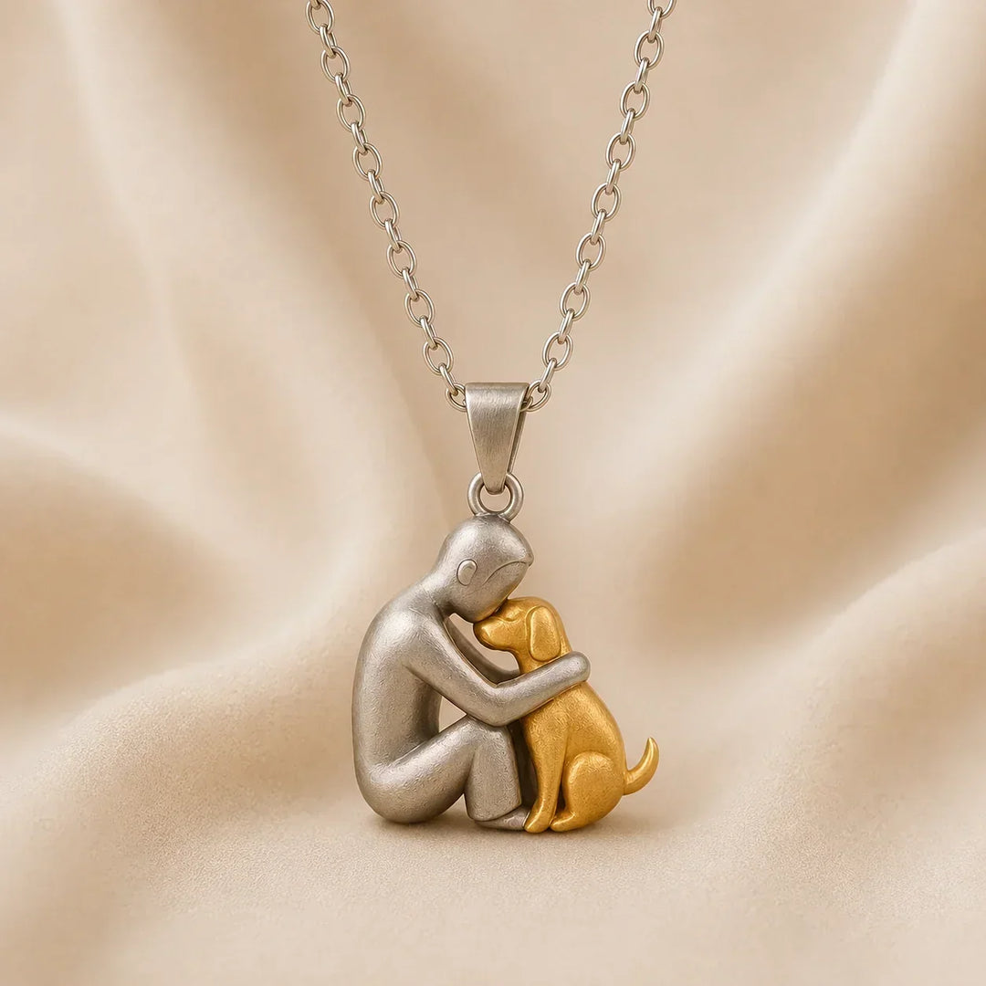Zijaanzicht van een mat zilverkleurige figuur die zijn hoofd tegen een goudkleurige hond legt, hangend aan een zilverkleurige ketting. 6