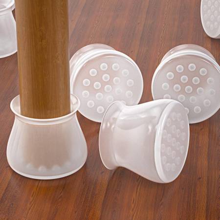 Close-up van doorschijnende siliconen dopjes op een houten vloer; de onderkant met noppen is zichtbaar en één dop zit om een stoelpoot. 2