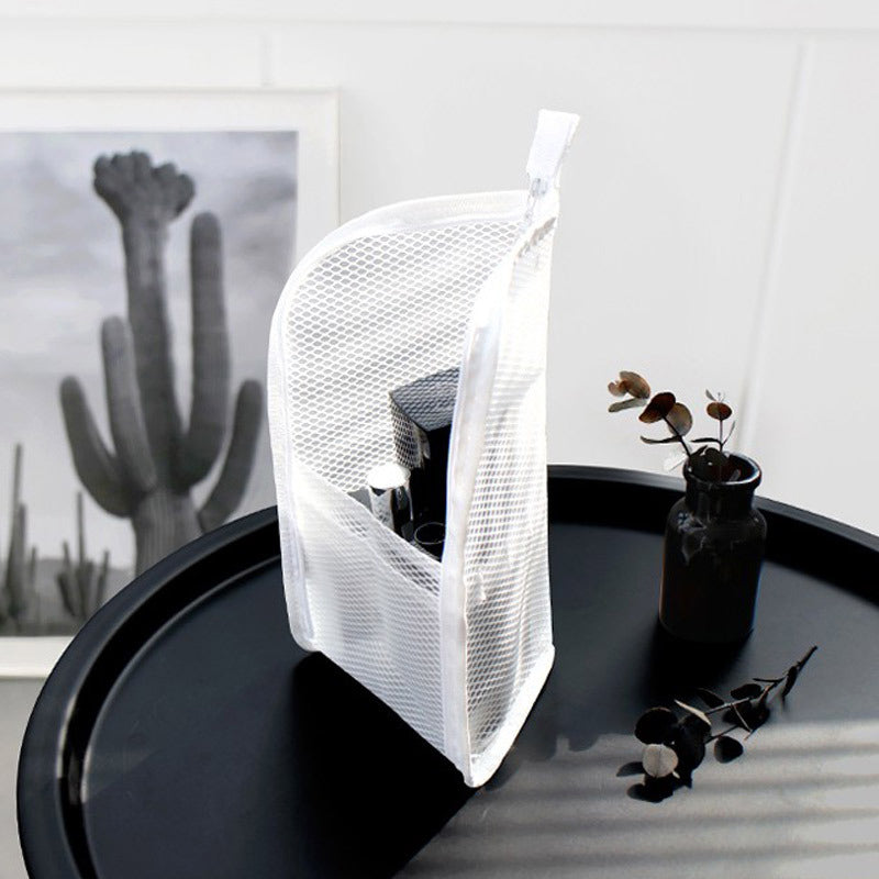 Witte mesh toilettas staat rechtop op een zwart tafeltje en toont de vakken met toiletspullen, naast een vaasje met takjes. 2