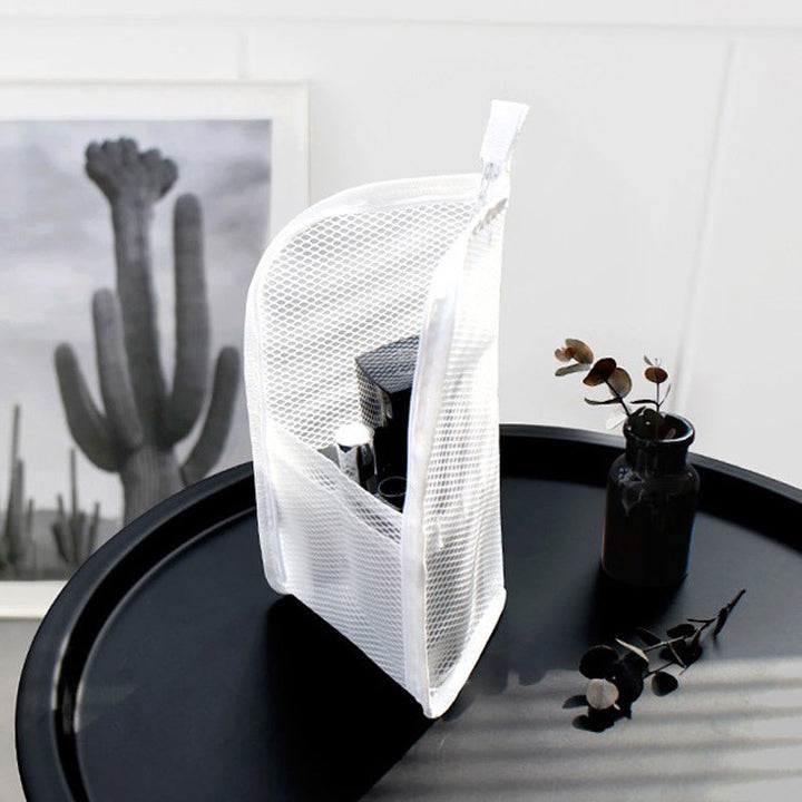 Witte mesh toilettas staat rechtop op een zwart tafeltje en toont de vakken met toiletspullen, naast een vaasje met takjes. 2