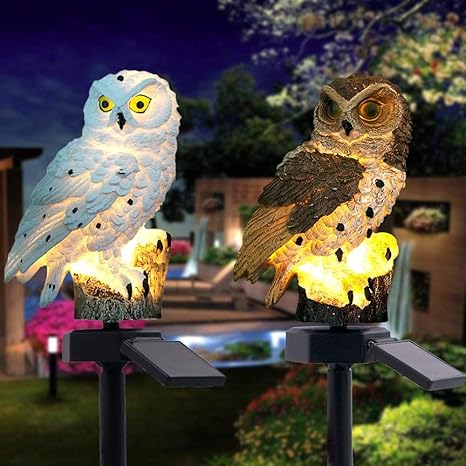 Een witte en een bruine uilenlamp naast elkaar, beide verlicht op prikstokken met zonnepaneel in een avondtuin. 17
