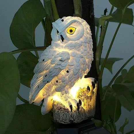 Close-up van een witte uilenlamp met gele ogen en warm licht, tussen groene bladeren. 8