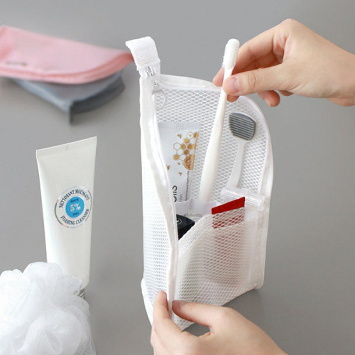 Handen openen de witte mesh toilettas en pakken een tandenborstel uit het vak, naast een tube en een badspons. 1