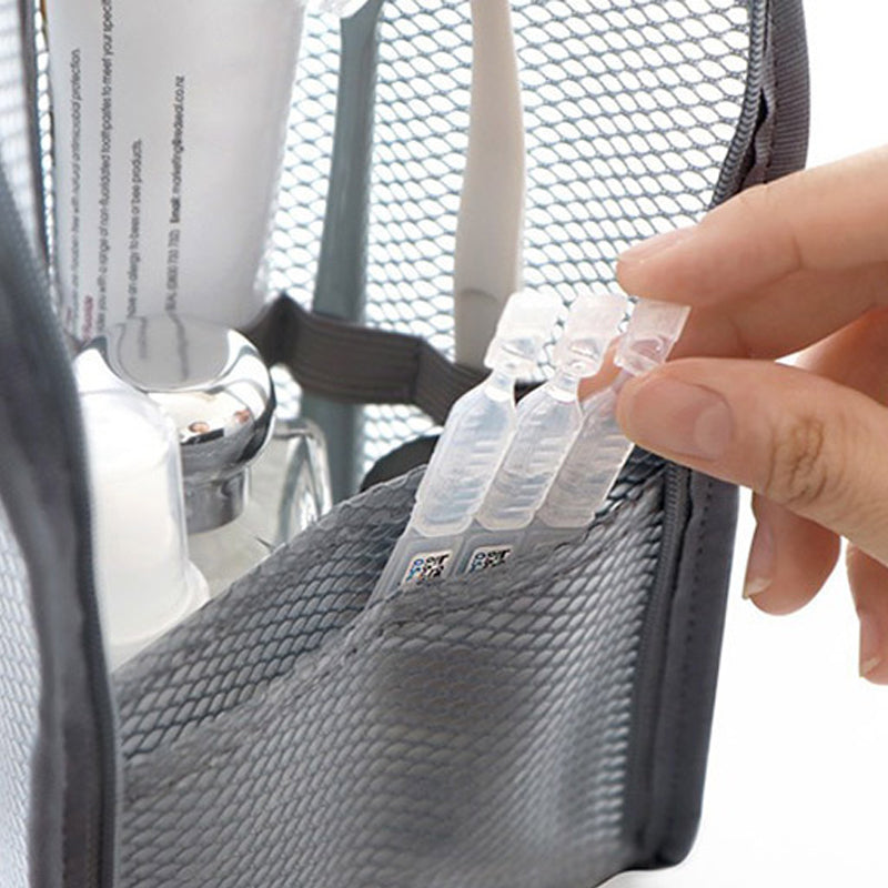 Close-up van het grijze mesh vak van de toilettas, waarin een hand kleine flacons en tandpasta vastheeft. 3