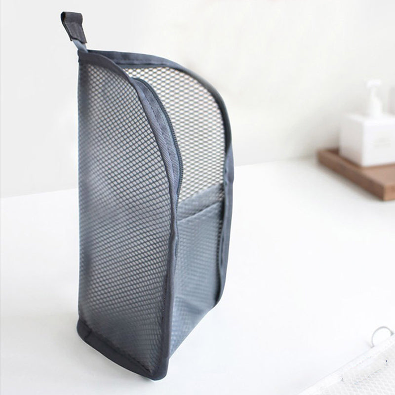 Grijze mesh toilettas staat rechtop op een wit blad, met ritssluiting, lus bovenaan en een buitenvak. 7