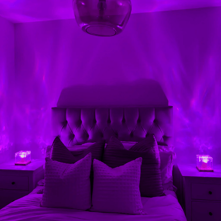 Dezelfde slaapkamer met twee kubuslampen op de nachtkastjes, nu in paars licht met zachte golvende projecties op de wanden. 3