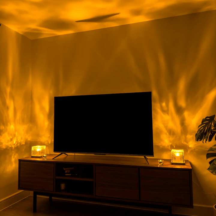 Twee kubuslampen op een tv-meubel in de woonkamer werpen warm geel golvend licht over de wanden en het plafond. 4