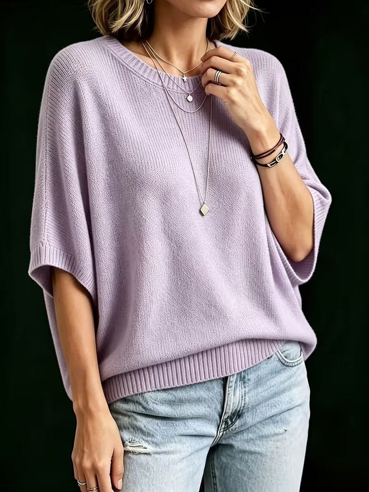 Lila gebreide top met ronde hals, model draagt gelaagde kettingen en armbanden, hand rust bij het sleutelbeen. 8