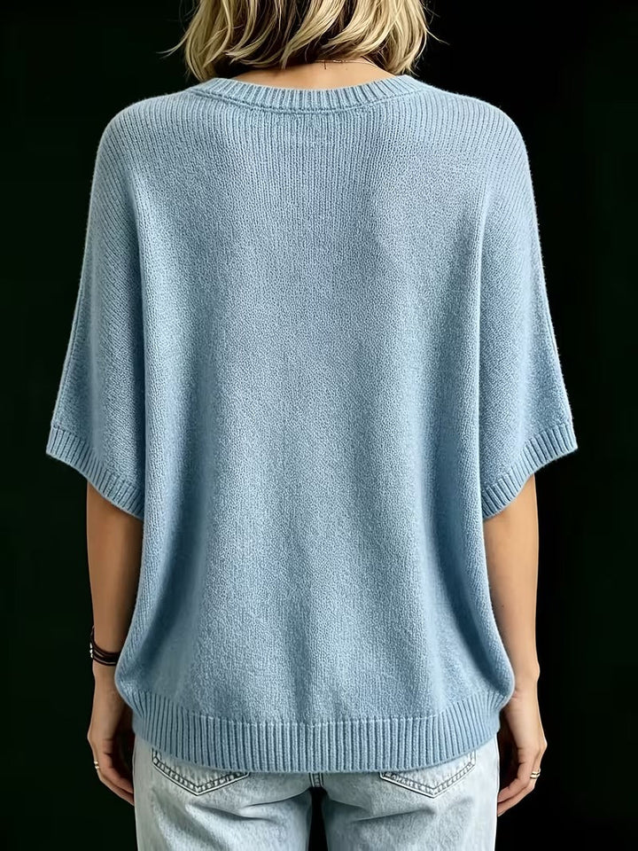 Achterkant van de lichtblauwe gebreide top met ronde hals, korte vleermuismouwen en geribbelde zoom, gedragen met jeans. 14