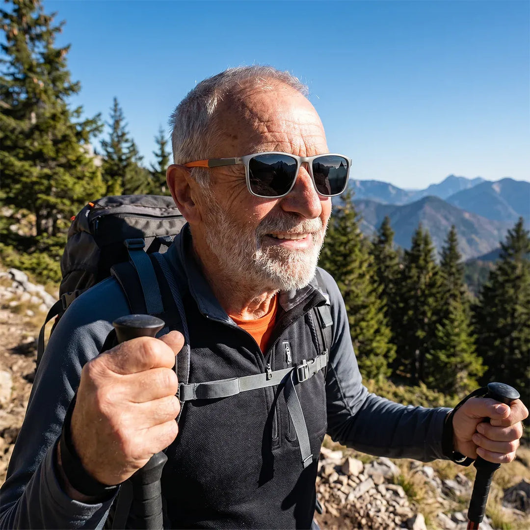 Oudere wandelaar met baard draagt de bril met donkere glazen en wandelstokken, met bergen en dennenbomen op de achtergrond. 5