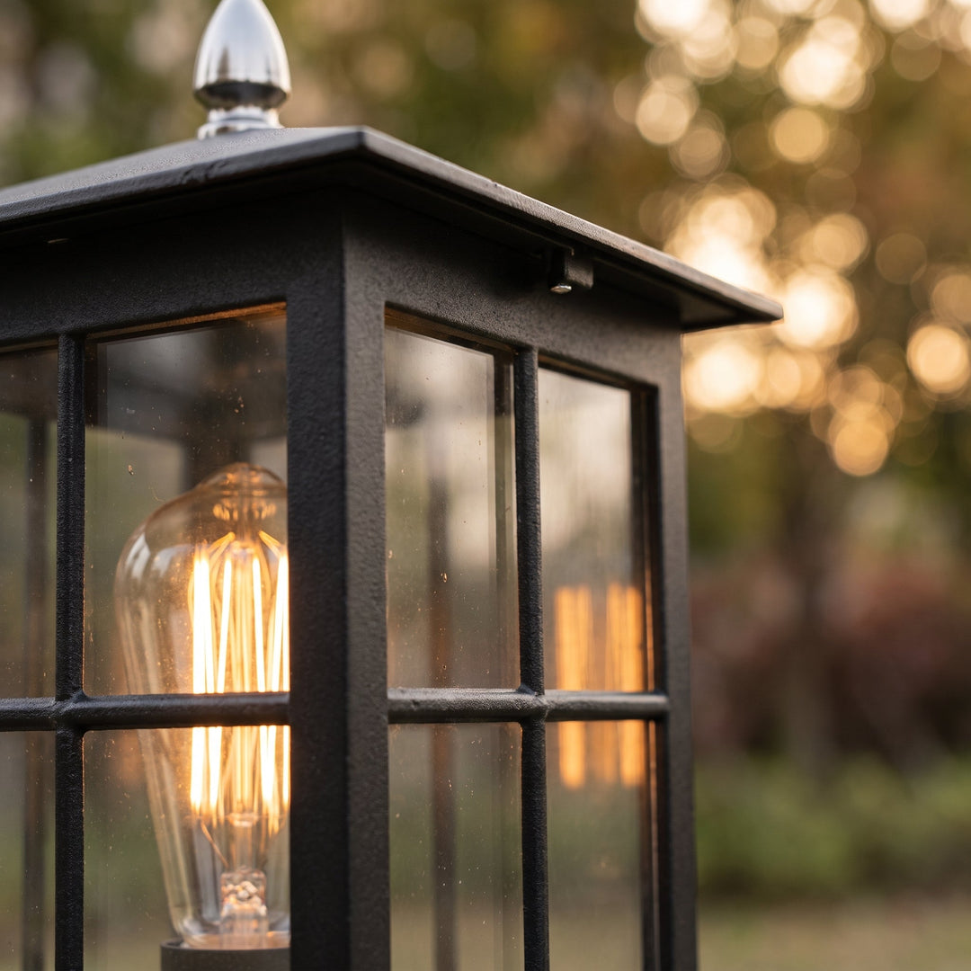 Close-up van de zwarte lamphouder met glazen ruitjes, een brandende filamentlamp en een zilverkleurige punt op het dak. 5