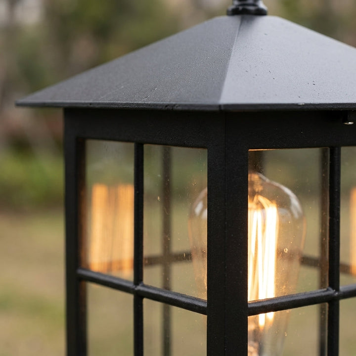 Close-up van het schuine zwarte dak en de raamverdeling van de lamp, met een gloeiende filamentlamp erachter. 6