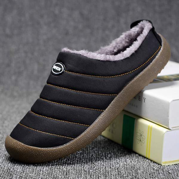 Zwarte pantoffel in zijaanzicht met pluche rand, schuin tegen boeken op grijs tapijt 10
