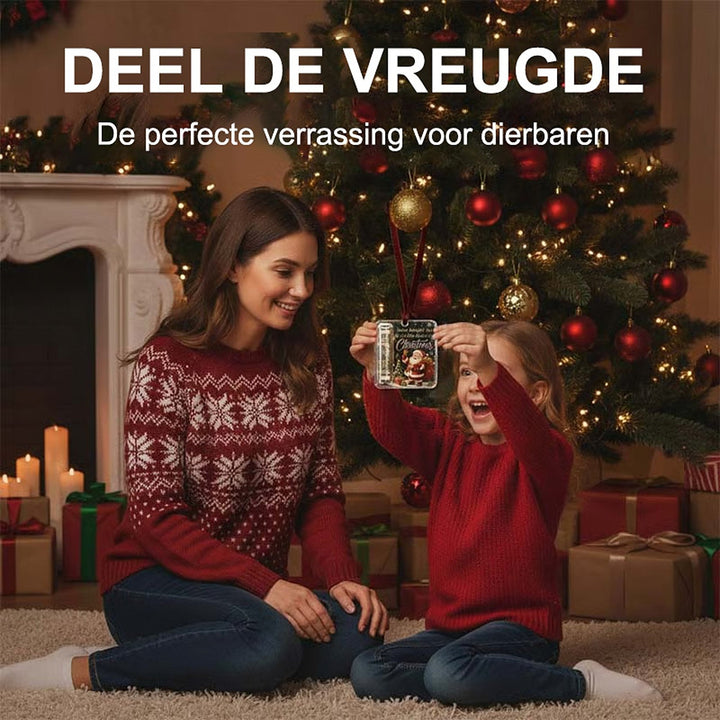 Moeder en kind zitten op een vloerkleed voor de kerstboom terwijl het meisje de hanger omhoog houdt en lacht. 3