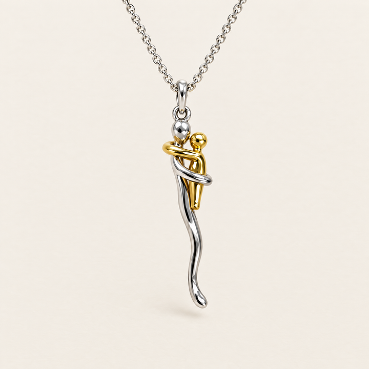 Zilverkleurige schakelketting met een hanger van twee omarmende figuurtjes, een grotere in zilvertint en een kleinere in goudtint, op een neutrale achtergrond. 1